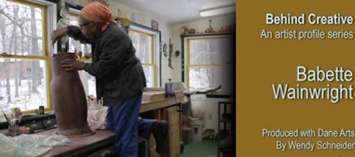Photo of a woman wearing an orange head scarf sculpting a large piece of clay in an artist studio 