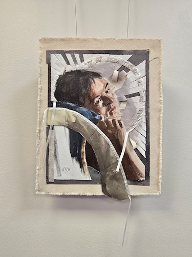 A square mixed media artwork hangs on a light-colored wall. The piece features a realistic portrait of a person’s face, partially covered by layered, folded, and stitched strips of fabric or paper that create a three dimensional effect. Radiating geometri
